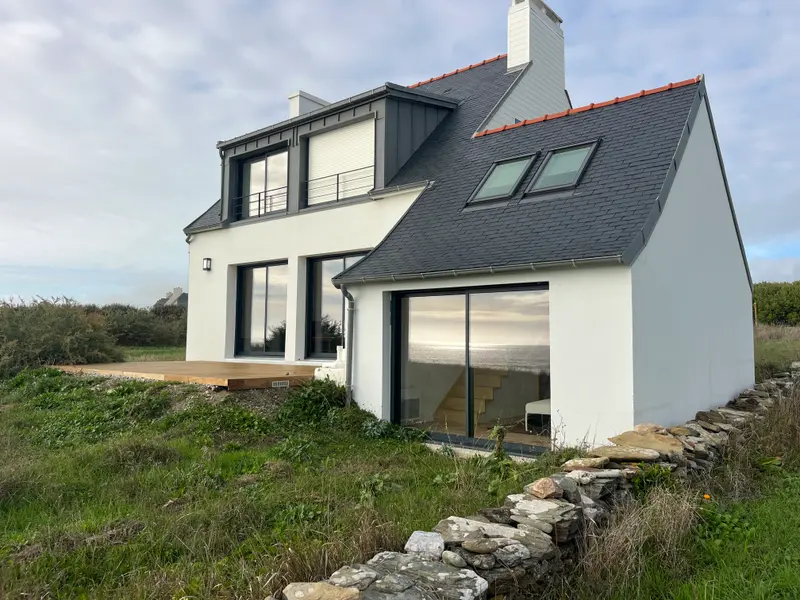 Maison bretonne aux murs blancs et grandes baies vitrées, face à la mer dans le Finistère